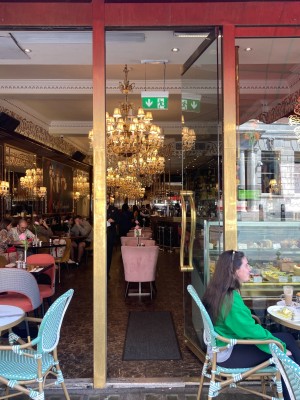 Glass door. Gold vertical handle on left, push to open. Outdoor tables and chairs to left and right of door.