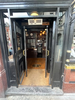 From right side of venue, facing venue. Double black wooden doors with glass panels ahead. Push fold metal handles from centre to open.