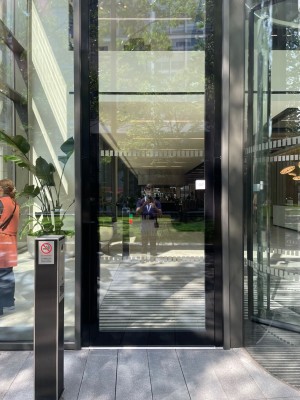 Single glass door in black metal frame. Opens inwards automatically on approach. Intercom on black post to left.