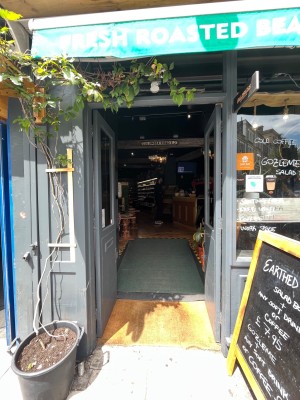 Double grey wooden doors with glass panels. Push gold metal handles from centre to open. Sandwich board to right.