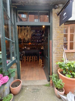 Dark green wooden door with glass panels. Push golden handle on left to open. Plants to left and right of door.