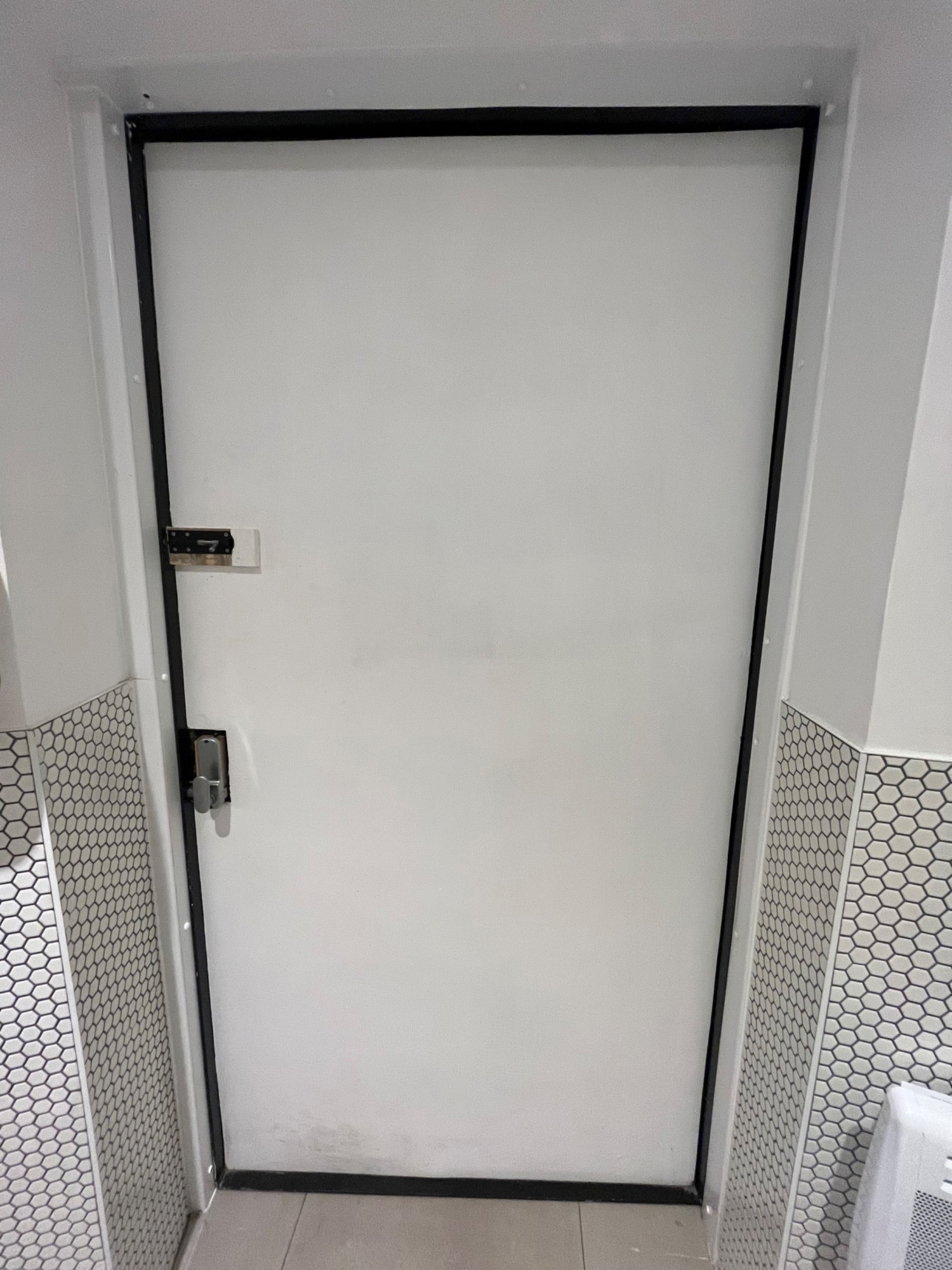 Facing back of toilet door. Single white wooden door. Silver sliding lock on left. Handle underneath. Pull to open.