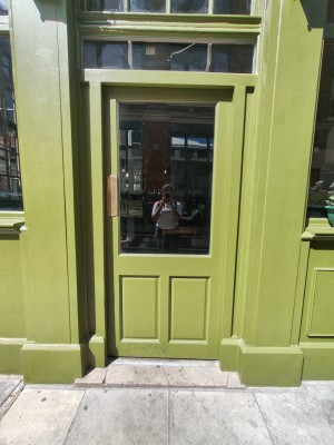 From side of venue facing left. Green framed door ahead. Push golden metal panel on left of door to open.