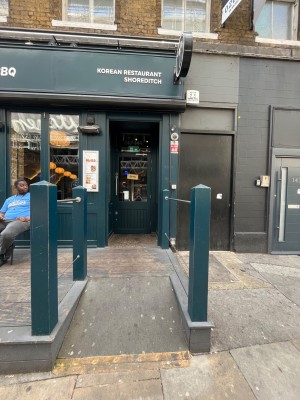 From pavement facing venue. Path to main entrance ahead between blue wooden posts.
