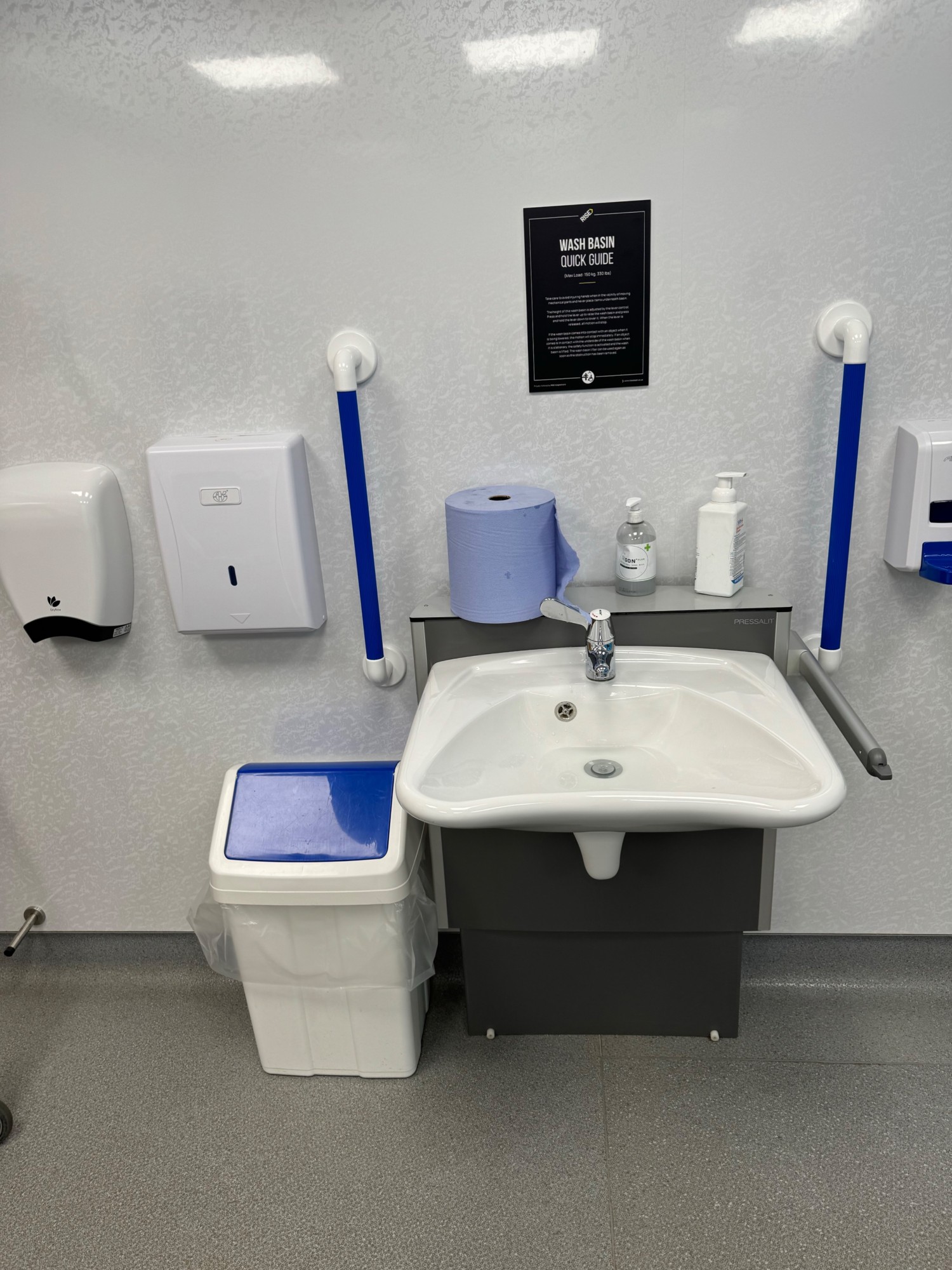 Height adjustable sink with bin to the left hand soap and hand towels on top of the sink and hand dryer to the left