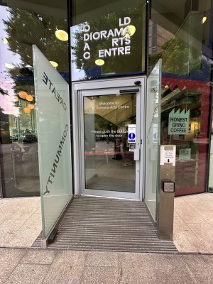 Glass door with grey frame. Grey handle on right. Door automatically opens outwards from right. Glass dividers to left and right of door.