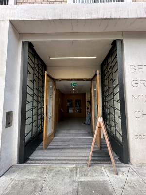 First set of glass doors with wood frames. Silver vertical handles in centre. Doors automatically open outwards from centre. A-frame to right of doors