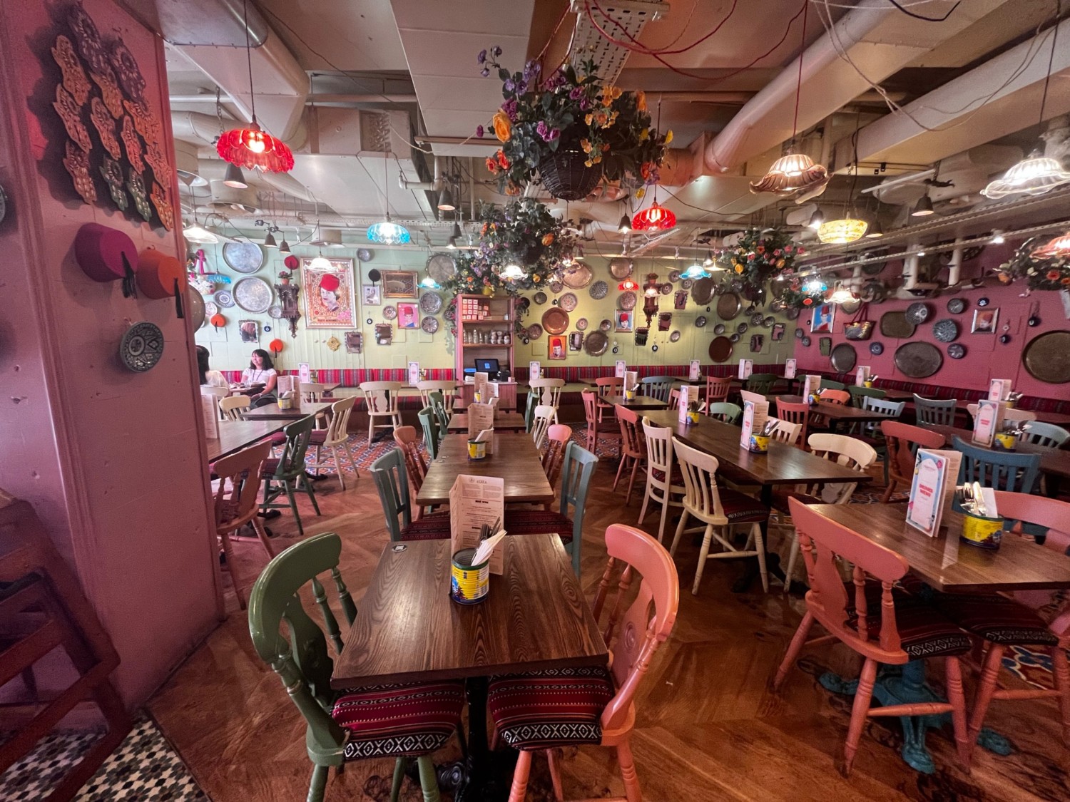 From plant facing left. Pink pillar to the left. Chairs to the far left. Half booth along the back wall. Chairs ahead.
