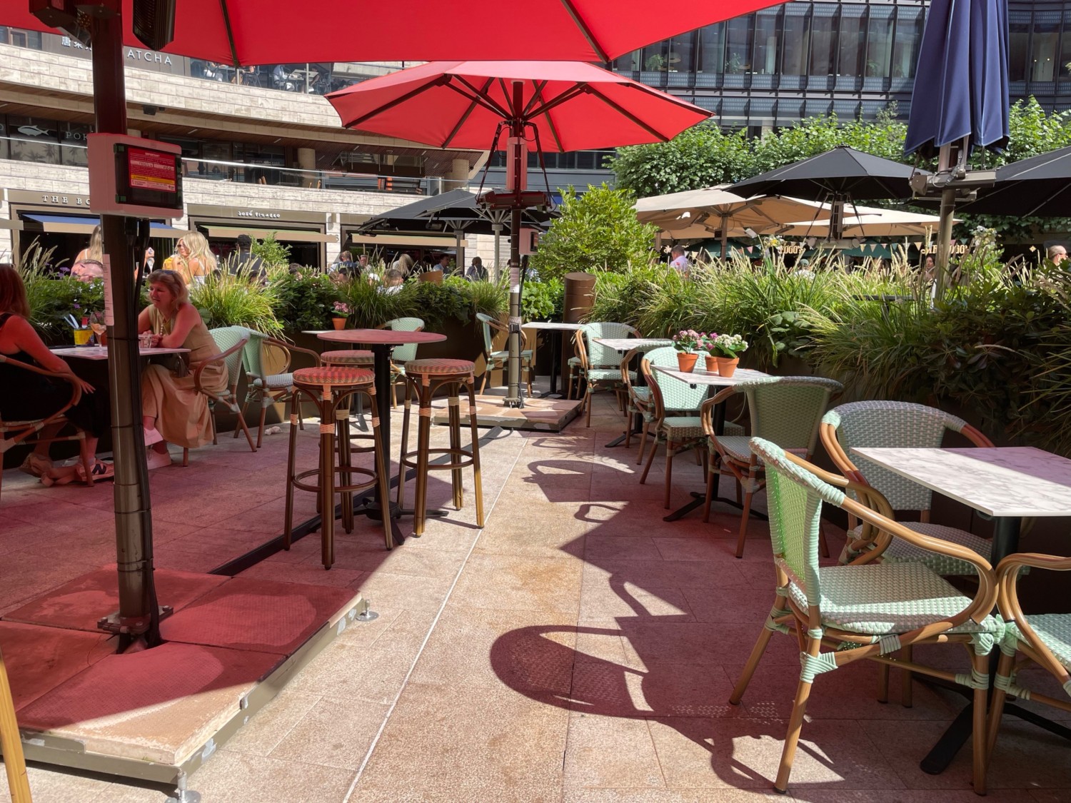 From steps, facing straight. Tables and chairs spread out ahead. Umbrella stand on left obstructing path between chairs.