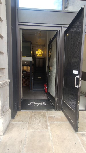 Single glass door with black metal frame. Push via black metal vertical handle on left to open.