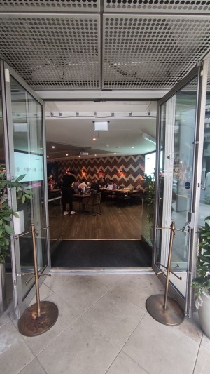 From right of venue facing left. Double glass doors with silver metal frames. Pull silver metal handles in centre to open. Bronze stands either side.