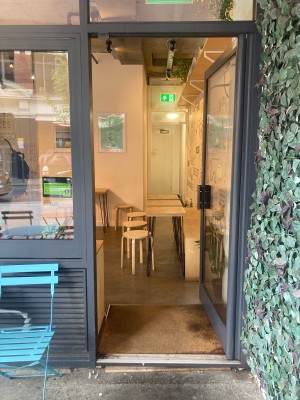 Glass door with grey frame. Push open via handle on left.