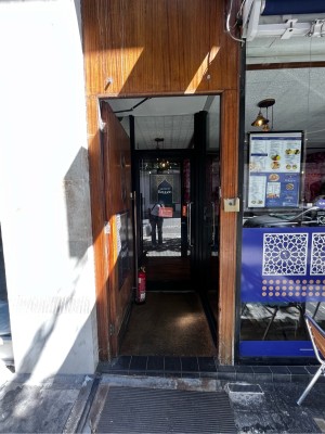 Facing wooden door. Push gold vertical metal handle on right to open.