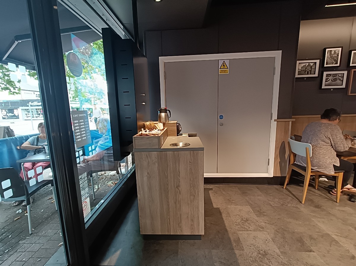 From entrance, looking left. Sugar station ahead. Path on right going right. Tables and chairs on back right.
