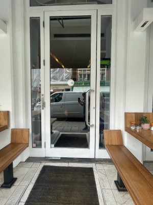 Single glass door with white frame. Silver metal handle to right. Pull to open. Benches to left and right of entrance.