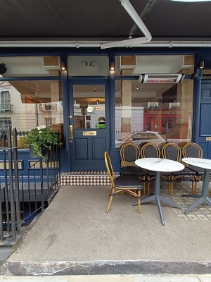 From street, facing venue. Tables and chairs on right. Path ahead. Door at back.