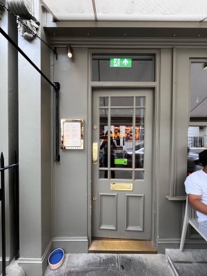 Facing door with green frames and glass window. Push gold metal area on left to open.