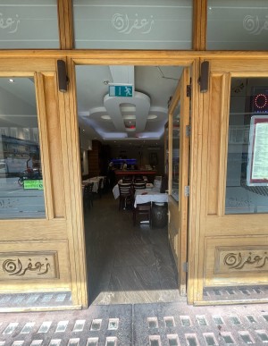 From pavement, facing straight. Light brown wooden and glass door ahead. Silver handle to right. Push to open.