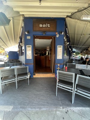 Facing entrance. Path in centre. Outdoor seating on either side. Wooden step at end of path.