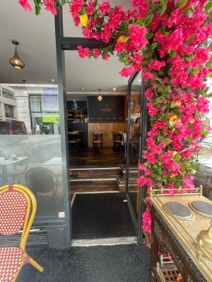 From pavement, facing straight. Glass door with black frame ahead. Black metal handle to left. Push to open.