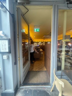 From pavement, facing straight. Glass door with grey frame ahead. Black metal handle on right. Push to open.