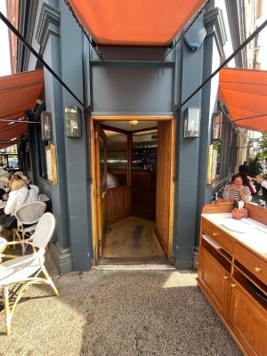 Single brown wooden door with glass panel on blue wall. Push gold metal handle from right to open.