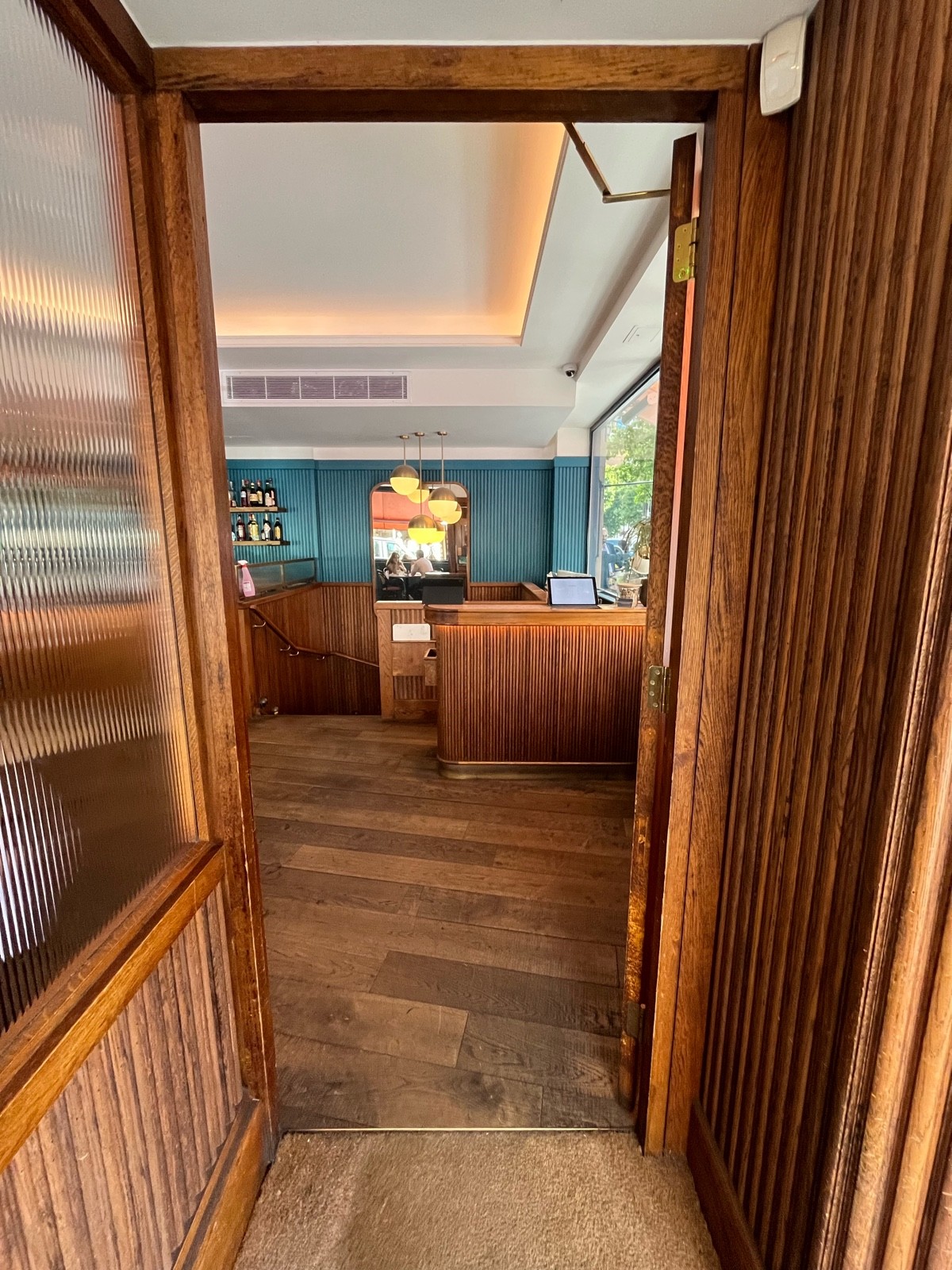 From door facing right. Second brown wooden door with glass window ahead. Push gold metal handle from left to open.