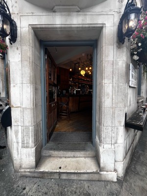 Facing entrance. Push black metal handle on right of door with wooden frames to open.
