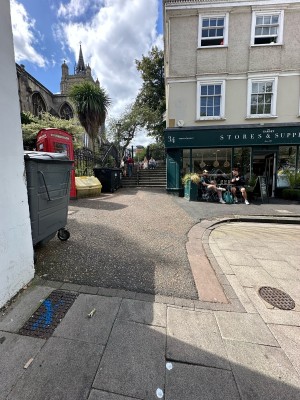From pavement, facing straight. Built-in ramp ahead. Bins and telephone box on left. Garnet shop ahead to right.