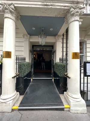 From pavement facing venue. Path to entrance ahead between two white stone pillars. Gold metal handrails on either side.