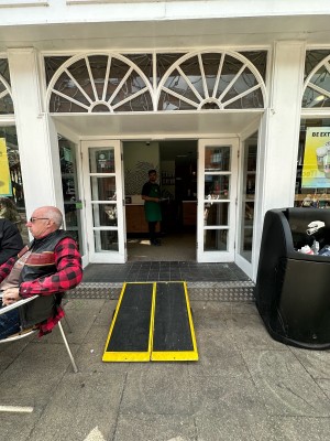 Ramp available upon request ahead. White and glass panelled doors ahead. Push from centre to open.