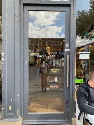 Glass door in grey wooden frame. Push from vertical silver metal handle on right.