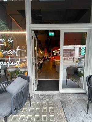 Facing entrance. White wood-framed glass door ahead. One step before entrance. Push brass handle on right to open.