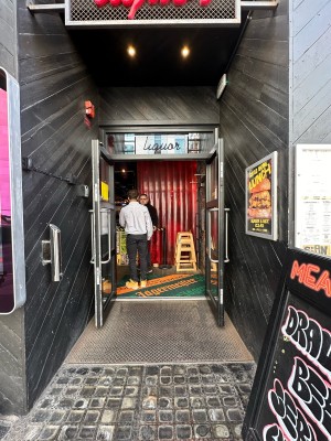 From pavement, facing straight. Glass doors with black frame. Silver vertical handles in centre, pull to open.