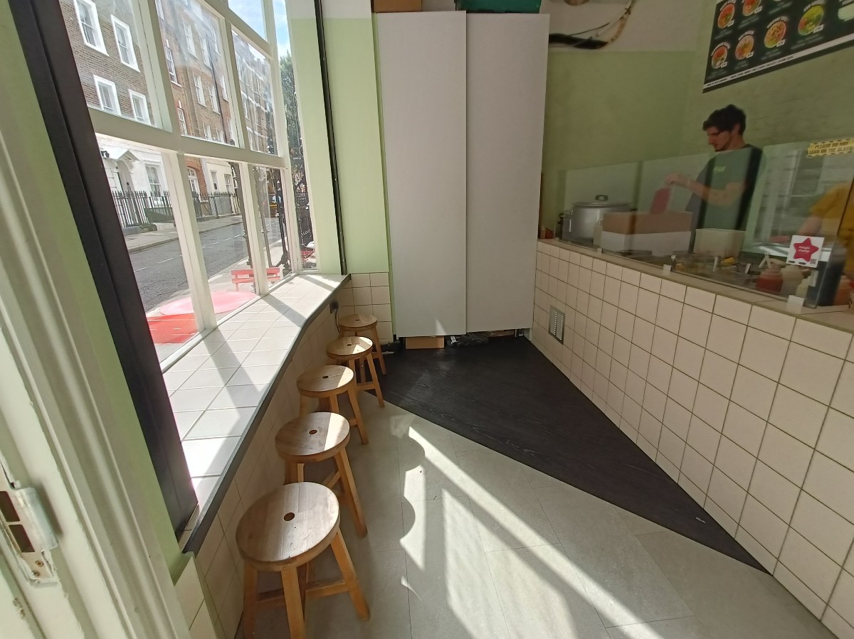 From entrance, looking left. Table and stools along left. Path in middle. Counter along right.
