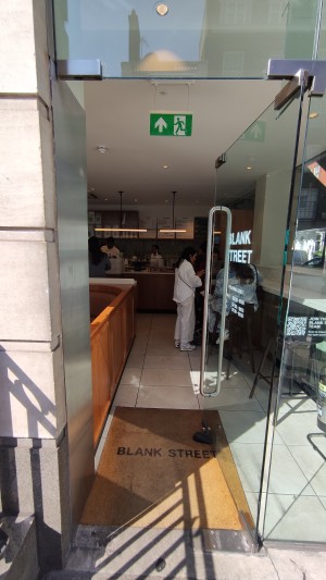 Glass door ahead. Push via vertical metal handle on left to open.