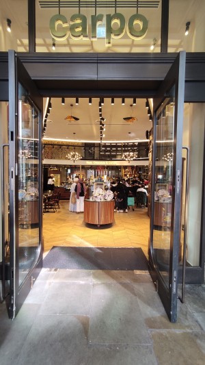 Glass doors with brown frames ahead. Pull via vertical metal handles in centre to open.
