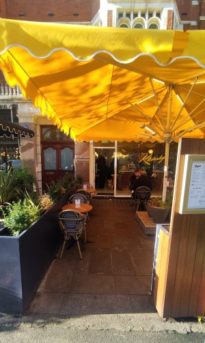 From pavement facing venue. Path to entrance ahead. Planter on left. Brown column on right.