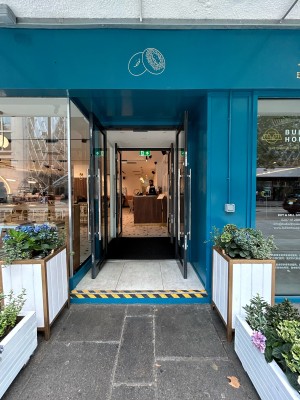 Open archway before preceding double glass doors with black frame. Pull long vertical silver handles in middle to open.