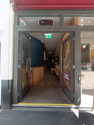 Glass doors with brown frame. Silver vertical handle in the middle. Push to open. Doorbell on right doorframe.
