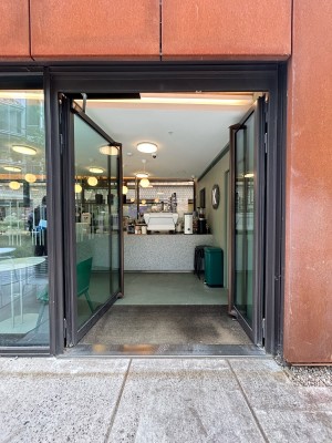 Double glass power assisted doors with dark brown metal frame. Long vertical dark brown metal frames along middle. Ask staff to unlock then push.