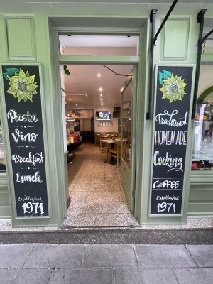 Glass door with green frame ahead. Metal handle to left. Push to open from left.