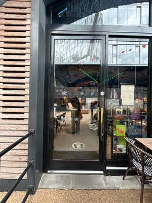 Single glass door with black metal frame. Pull vertical gold handle on right to open.