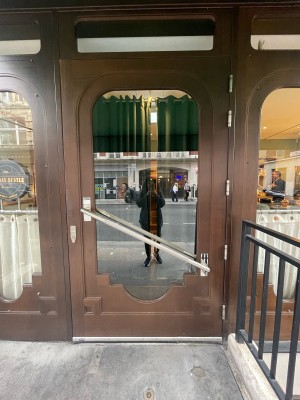 Glass door with wooden brown frame ahead. Diagonal silver handle in centre. Pull to open.