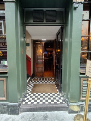 Facing single black entrance door. Push on left of door to open. Doorbell for assistance on left. Doormat on threshold of door.
