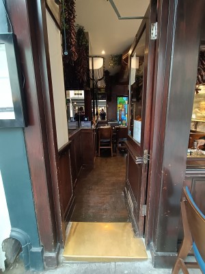 Glass door with brown frame. Golden pad on left. Push to open.