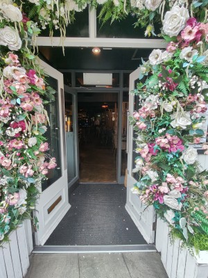 Facing white framed double glass doors. Push silver metal leaf on left and silver metal vertical handle on right to open.