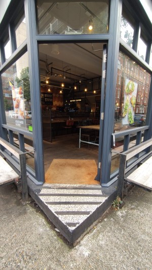 From sidewalk facing venue. Triangular stepup before door.