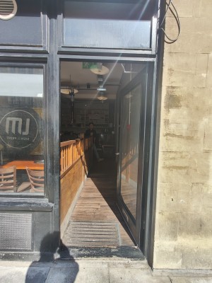 Facing black framed single glass door. Push silver metal handle on left to open.