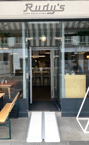 Access via glass door with glass frame. Push open via vertical metal handrail on left.